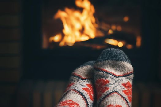 Girl resting and warming her feet by a burning fireplace in a country house on a winter evening. Selective focus