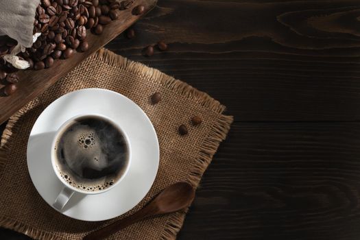 White cup of fresh hot coffee and coffee beans on the table, top view, flat lay, copyspace.