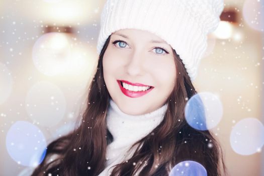 Christmas, people and winter holiday concept. Happy smiling woman wearing white knitted hat as closeup face xmas portrait, snow glitter and bokeh effect.