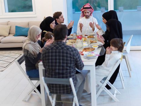 Muslim family making iftar dua to break fasting during Ramadan. Arabian people keeping hands in gesture for praying and thanking to Allah before traditional dinner