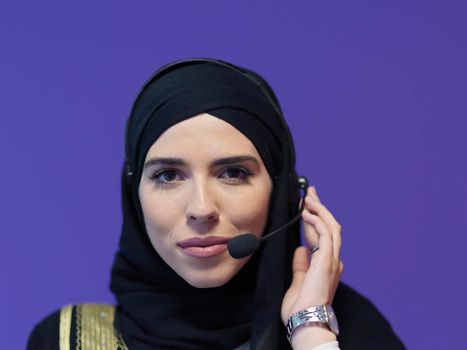 Portrait of young muslim woman with headphones working as call center operator isolated on purple background