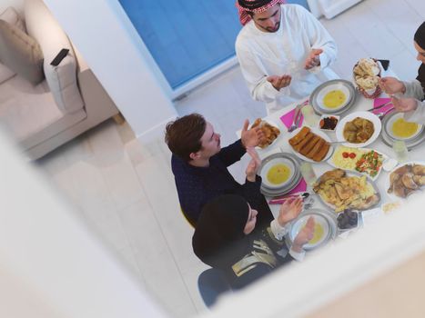 Top view of Muslim family making iftar dua to break fasting during Ramadan. Arabian people keeping hands in gesture for praying and thanking to Allah before traditional dinner