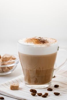 Latte coffee poured in layers with froth and a crispy chocolate top on a light kitchen table. Vertical image with copy space.