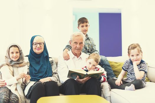 modern muslim family grandparents with grandchildren reading Quran and praying together on the sofa before iftar dinner during a ramadan feast at home