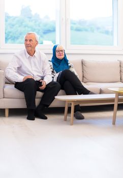 portrait of modern muslim senior couple sitting on the sofa before iftar dinner during a ramadan feast at home