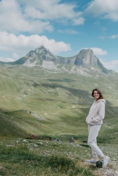 Hiker tourist girl standing on top of the mountain and enjoying valley view. Happy woman with her arms outstretched, freedom and happiness, achievement in mountains.