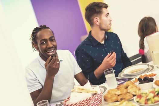 young african american man eating dates with modern multiethnic muslim family while enjoying iftar dinner together during a ramadan feast at home