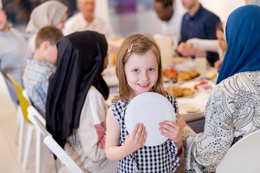 cute little girl enjoying iftar dinner together with modern multiethnic muslim family in the background  during a ramadan feast at home