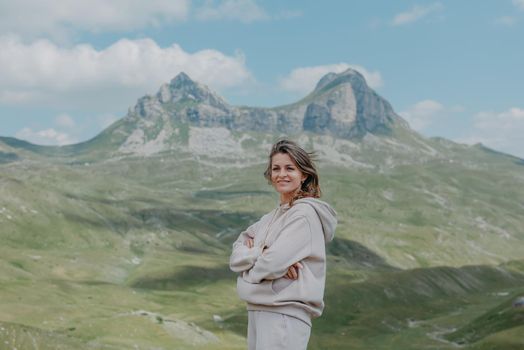 Hiker tourist girl standing on top of the mountain and enjoying valley view. Happy woman with her arms outstretched, freedom and happiness, achievement in mountains.