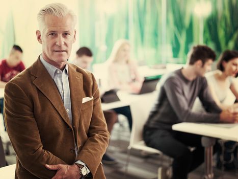 portrait of confident teacher in school classroom,  students group on class in background