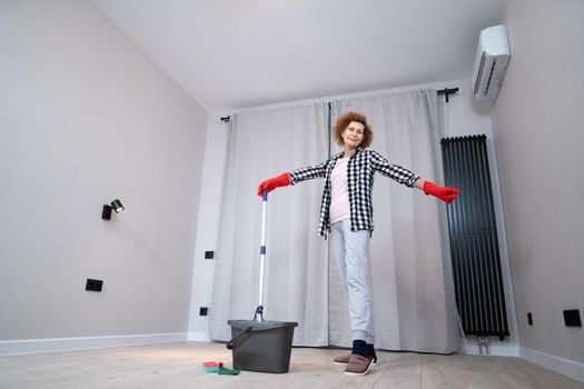 Jolly excited mature woman enjoying cleaning house, she dancing while washing floor. Happy elderly woman enjoying cleaning floors before moving to new apartment. Housework and housekeeping concept.