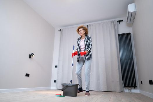 Jolly excited mature woman enjoying cleaning house, she dancing while washing floor. Happy elderly woman enjoying cleaning floors before moving to new apartment. Housework and housekeeping concept.