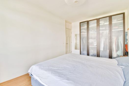 Comfortable bed covered with white blanket and located in light bedroom of modern apartment