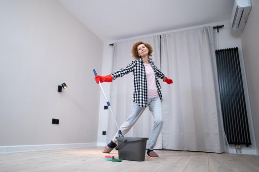 Jolly excited mature woman enjoying cleaning house, she dancing while washing floor. Happy elderly woman enjoying cleaning floors before moving to new apartment. Housework and housekeeping concept.