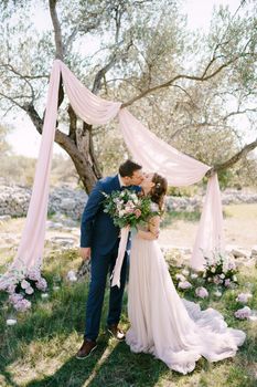 Groom and bride kiss under a tree in a green park. High quality photo