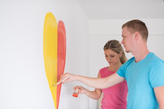 Young happy couple are painting a heart on the wall while doing repair at home.