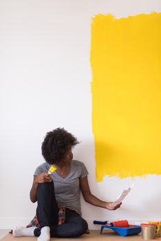 Portrait of a beautiful african american female painter sitting on floor near wall after painting.