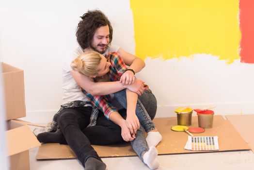 Happy young couple relaxing after painting a room in their new house on the floor