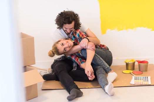 Happy young couple relaxing after painting a room in their new house on the floor