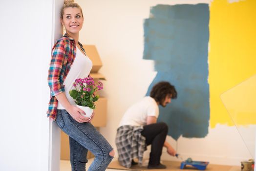 Happy couple doing home renovations, the man is painting the room and the woman hold the pot with flowers