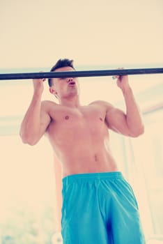 handsome young man in fitness gym lifting up and hanging while working on hands and back muscles