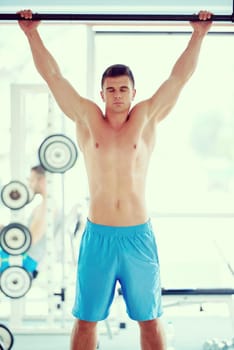 handsome young man in fitness gym lifting up and hanging while working on hands and back muscles