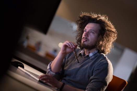 Young man working on computer at night in dark office. The designer works in the later time.