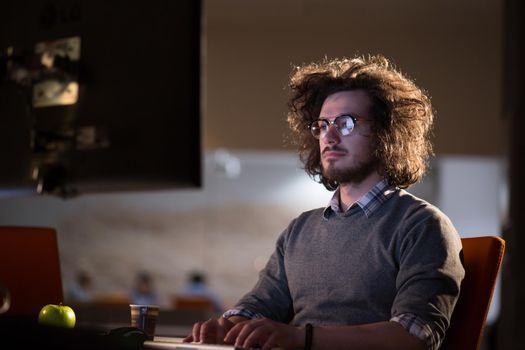 Young man working on computer at night in dark office. The designer works in the later time.