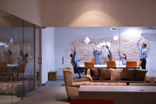 Group of young business people throwing documents and looking happy while celebrating success at their working places in night office