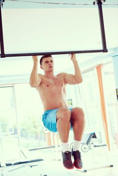 handsome young man in fitness gym lifting up and hanging while working on hands and back muscles