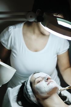 Young beautiful woman receiving cosmetic facial mask in spa beauty salon and relax