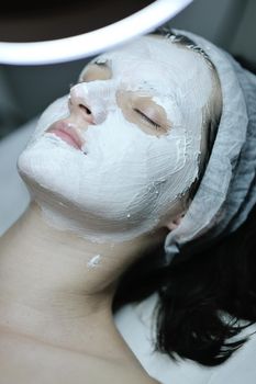 Young beautiful woman receiving cosmetic facial mask in spa beauty salon and relax