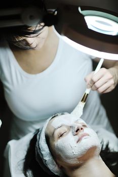 Young beautiful woman receiving cosmetic facial mask in spa beauty salon and relax