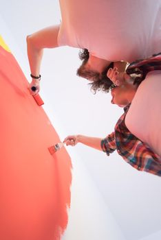 happy smiling young couple painting interior wall of new house