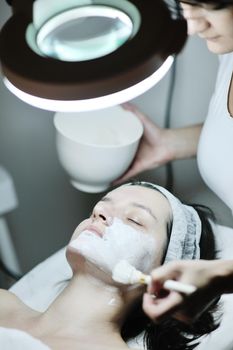 Young beautiful woman receiving cosmetic facial mask in spa beauty salon and relax