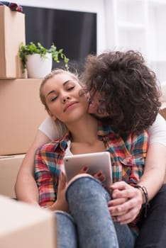 Relaxing in new house. Cheerful young couple sitting on the floor while cardboard boxes laying all around them