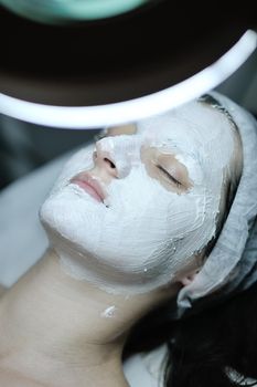 Young beautiful woman receiving cosmetic facial mask in spa beauty salon and relax