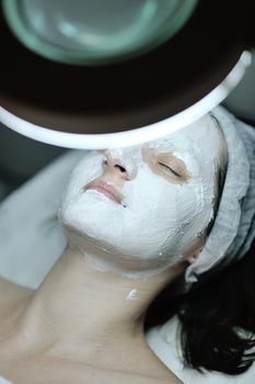 Young beautiful woman receiving cosmetic facial mask in spa beauty salon and relax