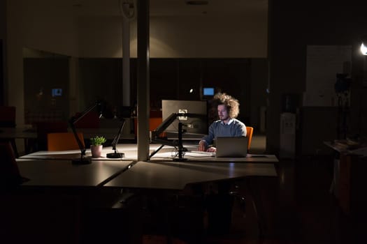 Young man working on computer at night in dark office. The designer works in the later time.