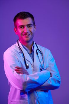 Coronavirus covid-19 danger alert Portrait of hero in white coat.  Cheerful smiling young doctor with stethoscope in medical hospital standing against blue and pink background.