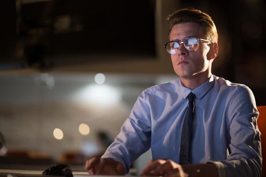 Young man working on computer at night in dark office. The designer works in the later time.