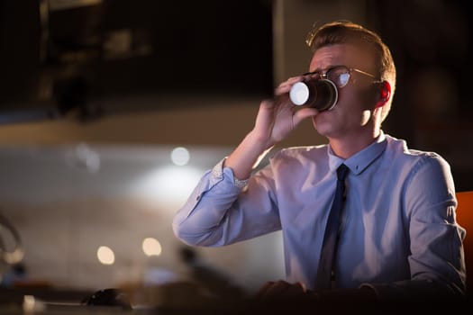 Tired businessman working late doing overtime in office at night drinking coffee to go on.