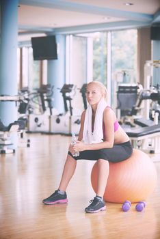 young healthy blonde woman drinking water  in fitness gym while sitting on pilates ball