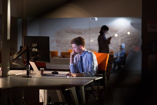 Young man working on computer at night in dark office. The designer works in the later time.