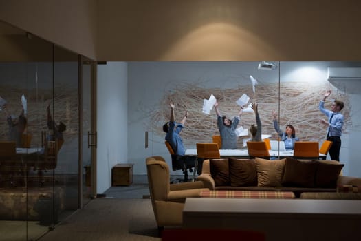 Group of young business people throwing documents and looking happy while celebrating success at their working places in night office