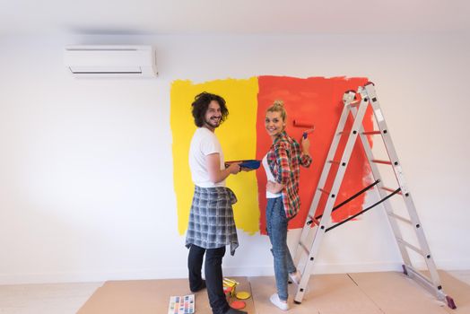 happy smiling young couple painting interior wall of new house