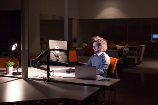 Young man working on computer at night in dark office. The designer works in the later time.