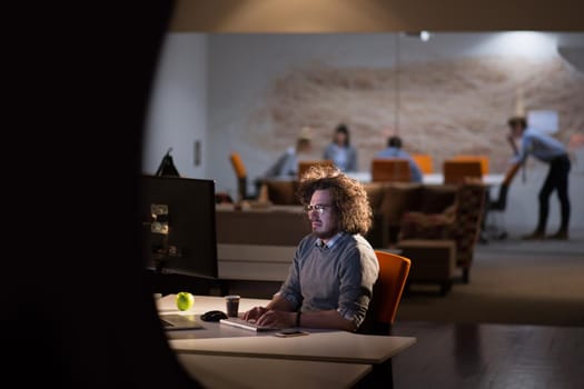 Young man working on computer at night in dark office. The designer works in the later time.