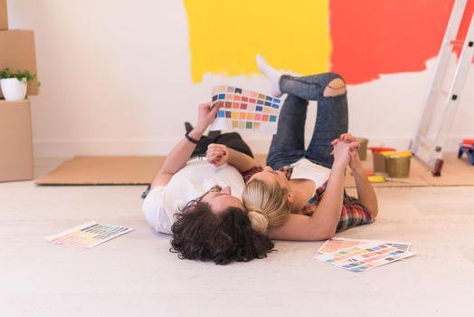 Happy young couple relaxing after painting a room in their new house on the floor