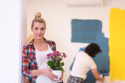 Happy couple doing home renovations, the man is painting the room and the woman hold the pot with flowers